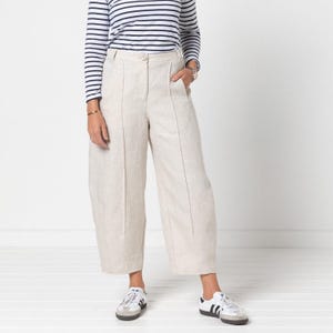 Puede incluir: Pantalón de lino beige de pierna ancha con pliegues. El pantalón tiene cierre de botón y cremallera y está cortado por encima del tobillo.