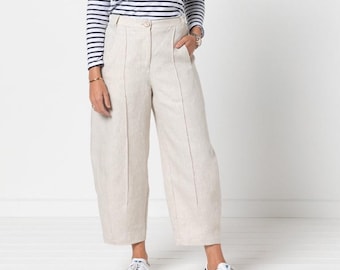 Op de afbeelding: Een shirt met lange mouwen en een horizontaal marineblauw en wit streeppatroon, gecombineerd met een beige broek met hoge taille, wijde pijpen en een naad in het midden. De outfit wordt afgemaakt met witte sportschoenen met zwarte strepen.