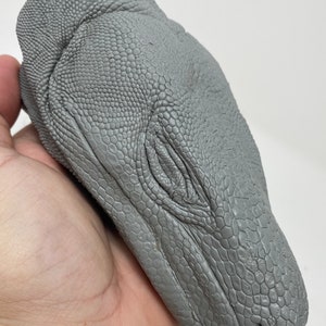 Könnte beinhalten: Ein grauer, detaillierter, geformter Kopf eines Komodowarans mit einer strukturierten, schuppigen Oberfläche.