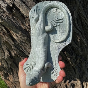 Puede incluir: Una escultura de pared de lagarto impresa en 3D de color gris con una superficie texturizada.