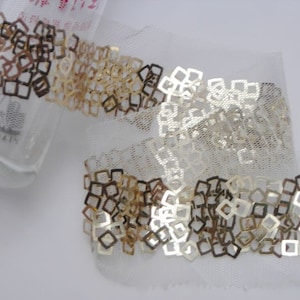 May include: Gold and silver square sequins on a white mesh trim. The trim is approximately 2.5 cm wide.
