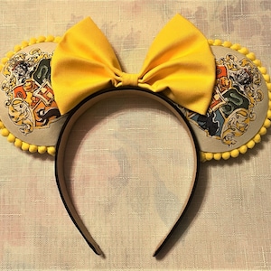 May include: A yellow bow headband with two round ears featuring the Hogwarts crest. The ears are trimmed with yellow pom-poms. The headband is black.