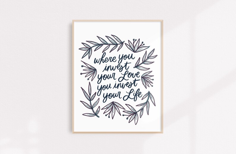 Może przedstawiać: Wydruk w ramie z białym tłem i czarną kaligrafią, kt&oacute;ra brzmi "where you invest your love you invest your life". Kaligrafia jest otoczona wieńcem stylizowanych liści i kwiat&oacute;w w odcieniach niebieskiego i fioletowego.