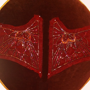 Peut inclure: Deux panneaux de tissu en velours rouge avec des motifs perlés complexes. Les motifs sont symétriques et présentent un motif géométrique avec un motif central de fleur stylisée.