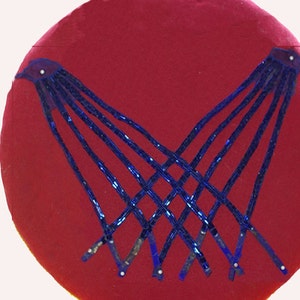 Peut inclure: Un coussin circulaire rouge avec un motif de perles bleues. Les perles sont disposées en un motif symétrique, créant un design géométrique.