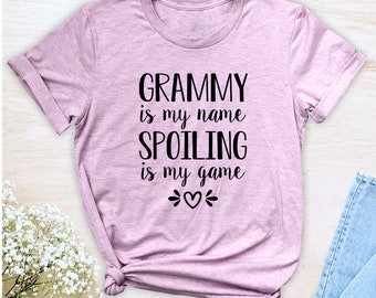 Könnte beinhalten: Ein hellrosa T-Shirt mit dem Text "GRAMMY is my name SPOILING is my game" in schwarzer Schrift mit zwei kleinen Herzen.
