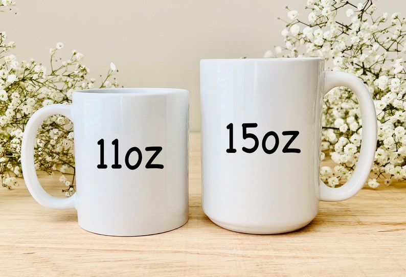 Pode incluir: Duas canecas de cer&acirc;mica branca com texto preto. A caneca menor diz "11oz" e a caneca maior diz "15oz".