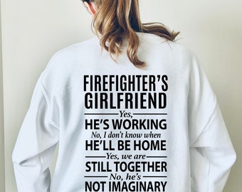 May include: White sweatshirt with black text that reads "FIREFIGHTER'S GIRLFRIEND - Yes, HE'S WORKING No, I don't know when HE'LL BE HOME - Yes, we are STILL TOGETHER - No, he's NOT IMAGINARY"