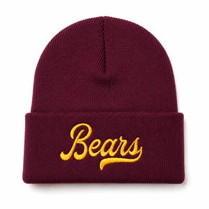 May include: A deep maroon knit beanie featuring a folded cuff. The word Bears is embroidered across the front of the cuff in a bright yellow cursive script font. The hat is constructed from a ribbed fabric with a vertical texture throughout.