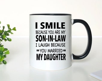 May include: White ceramic coffee mug with a black rim and handle. The mug has black text that reads "I smile because you are my son-in-law. I laugh because you married my daughter."