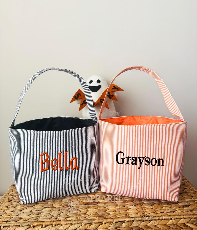 May include: Two striped Halloween treat bags. One is navy and white with orange embroidery that says "Bella". The other is peach and white with black embroidery that says "Grayson". Both have handles.