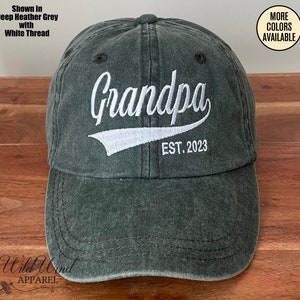 May include: A dark green baseball cap with white embroidery that reads "Grandpa EST. 2023".