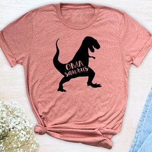 May include: A pink t-shirt with a black dinosaur silhouette and the text "OMA saurus" in pink.