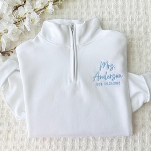 May include: White half-zip sweatshirt with blue embroidery that reads "Mrs. Anderson Est. 05.29.2025"