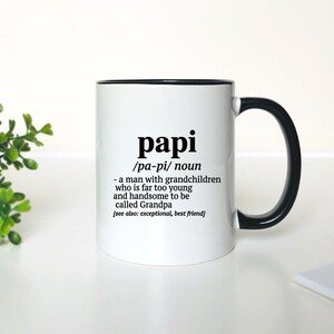 May include: White ceramic mug with a black rim and handle. The mug has a black graphic that reads "papi /pa-pi/ noun - a man with grandchildren who is far too young and handsome to be called Grandpa [see also: exceptional, best friend]"