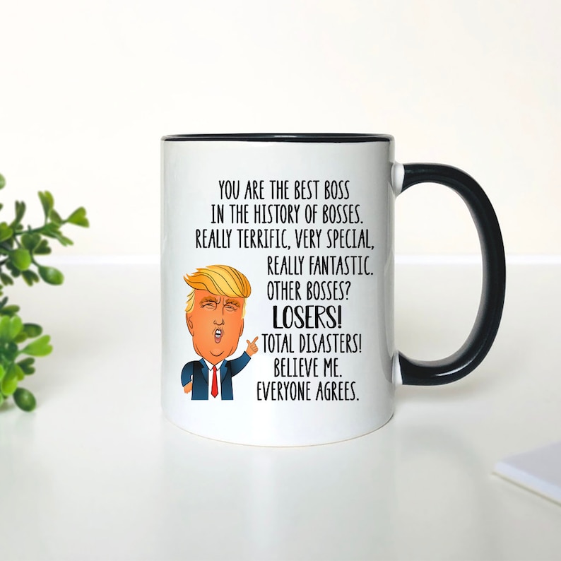 Pode incluir: Caneca de cer&acirc;mica branca com borda e al&ccedil;a pretas. A caneca apresenta uma imagem de desenho animado de Donald Trump com o texto "You are the best boss in the history of bosses. Really terrific, very special, really fantastic. Other bosses? Losers! Total disasters! Believe me. Everyone agrees."