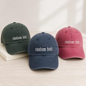 May include: Three baseball caps in dark green, navy blue, and faded red, each featuring a six-panel construction with a curved brim and an adjustable strap. The front of each cap is embroidered with the white lowercase text custom text.
