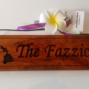 May include: A wooden sign with the text "The Fazzio's" and an outline of the Hawaiian islands. The sign is made of Koa wood and is handmade in Hawaii.
