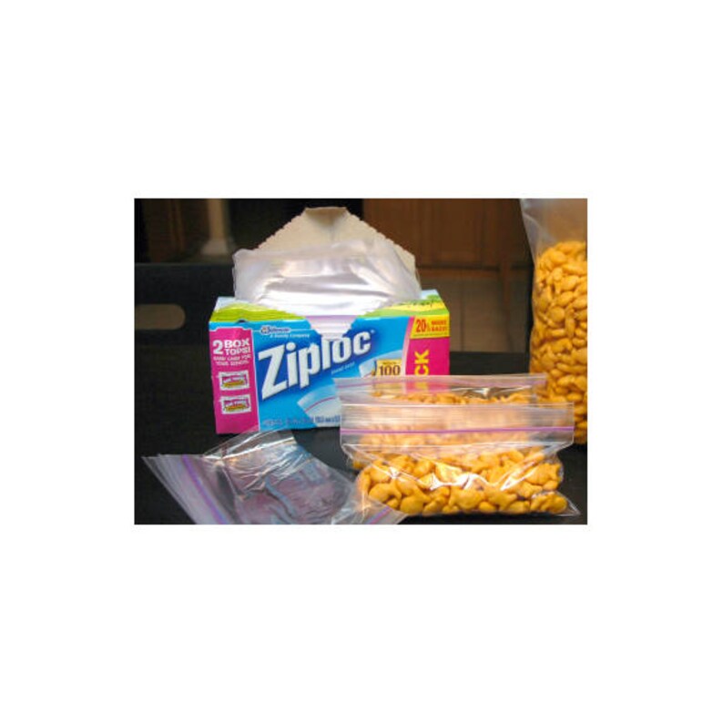 Pode incluir: Uma caixa de sacos de armazenamento da marca Ziploc com embalagem azul, verde e rosa, contendo sacos de pl&aacute;stico transparentes. V&aacute;rios sacos s&atilde;o vis&iacute;veis, incluindo um cheio de bolachas salgadas laranja em forma de peixe e um saco vazio.