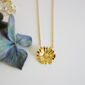 May include: A gold chain necklace with a delicate gold daisy pendant. The daisy has a textured center and petals.