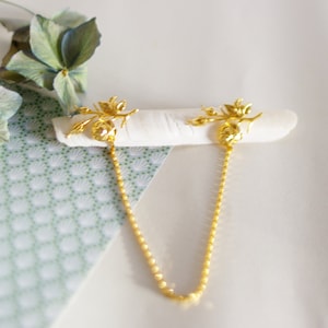 Peut inclure: Un collier en chaîne dorée avec deux pendentifs en forme de rose. Les pendentifs sont attachés à la chaîne par une boucle et présentent un motif floral détaillé.
