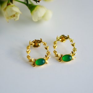 Puede incluir: Un par de pendientes de oro con una piedra verde engastada en un diseño de corona.