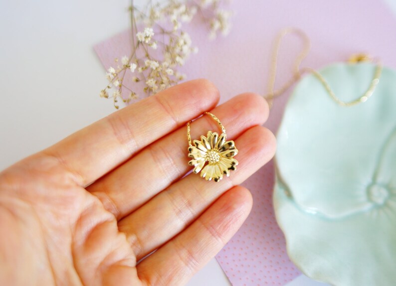 May include: A gold-toned necklace with a delicate chain and a flower pendant. The flower pendant is a detailed design with a textured surface.