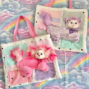 May include: Two tote bags with pink handles and plush animal appliqués. One bag features a pink poodle-like creature, the other a purple cat-like figure. The bags have patchwork designs with pastel colors and black polka dots.