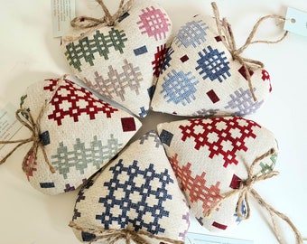 May include: Five handmade heart-shaped pillows with a woven pattern in shades of red, blue, green, and beige. The pillows are tied with twine.