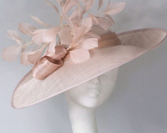 May include: A wide-brimmed hat made of a light beige fabric with a large, blush-colored feather embellishment.
