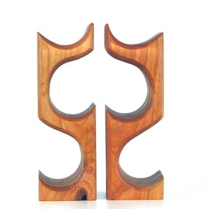 May include: Two wooden wine bottle holders. Each holder is made of light brown wood with a curved design. The holders have two circular openings for the bottles. The design is modern and minimalist.
