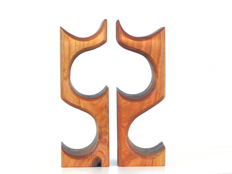 May include: Two wooden wine bottle holders. Each holder is made of light brown wood with a curved design. The holders have two circular openings for the bottles. The design is modern and minimalist.