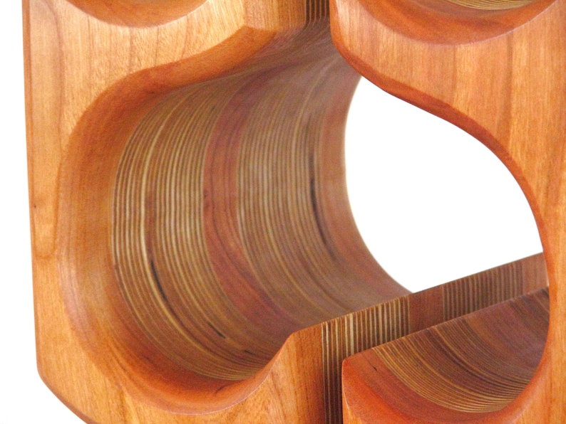 May include: Wooden wine rack with a layered design. The rack is made of light and dark brown wood, with curved openings for bottles. The design features a series of curved, layered wooden elements.