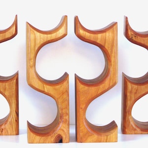 May include: Four wooden wine bottle holders. Each holder is a light brown color with a curved design. The holders are made of wood and have a smooth finish. The holders are designed to hold wine bottles.