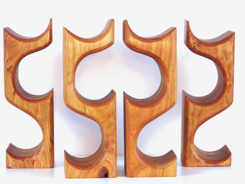 May include: Four wooden wine bottle holders. Each holder is a light brown color with a curved design. The holders are made of wood and have a smooth finish. The holders are designed to hold wine bottles.