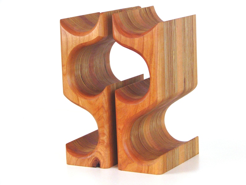 May include: A wooden wine rack with a unique, curved design. The rack is made of light brown wood and features openings for holding wine bottles. The design is modern and sculptural, suitable for home decor.