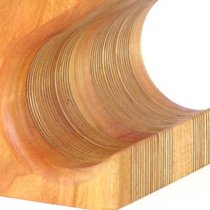 May include: Wooden wine rack with a curved design. The rack is made of light brown wood with a series of curved, layered slats. The design is a modern take on a classic wine storage solution.