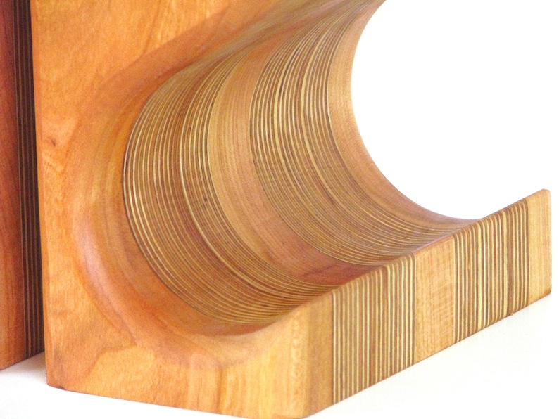 May include: Wooden wine rack with a curved design. The rack is made of light brown wood with a series of curved, layered slats. The design is a modern take on a classic wine storage solution.