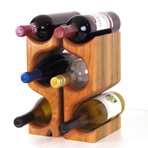 May include: A wooden wine rack holding six bottles of wine. The rack is made of light brown wood and has a unique, curved design. The wine bottles are various colors, including red, white, and blue.