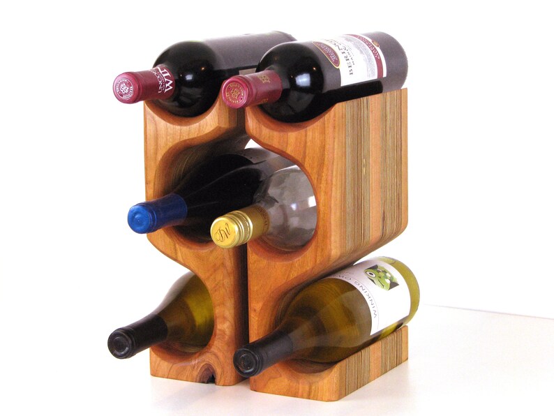 May include: A wooden wine rack holding six bottles of wine. The rack is made of light brown wood and has a unique, curved design. The wine bottles are various colors, including red, white, and blue.