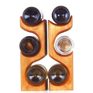 May include: A wooden wine rack with a natural finish, holding six wine bottles. The rack has a unique, curved design with slots to cradle the bottles. The bottles are brown and clear glass.