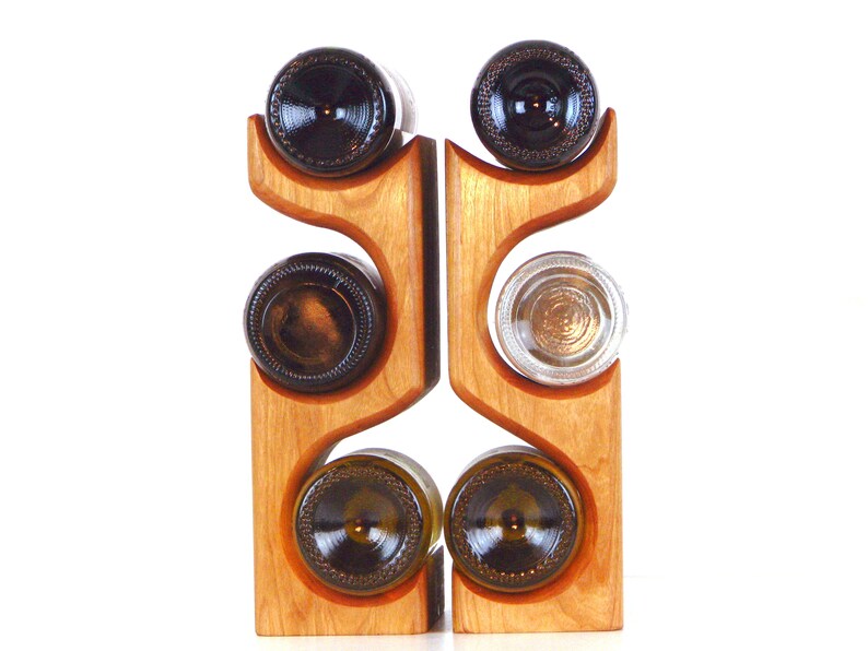 May include: A wooden wine rack with a natural finish, holding six wine bottles. The rack has a unique, curved design with slots to cradle the bottles. The bottles are brown and clear glass.