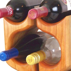 May include: A wooden wine rack holding several bottles of wine. The rack is made of light brown wood and has curved openings to hold the bottles. The wine bottles have red and blue caps.