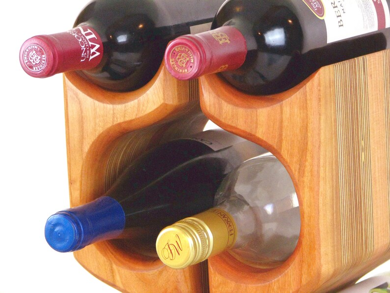 May include: A wooden wine rack holding several bottles of wine. The rack is made of light brown wood and has curved openings to hold the bottles. The wine bottles have red and blue caps.