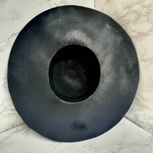 Puede incluir: Un sombrero negro de ala ancha hecho de fieltro. El sombrero tiene una corona grande y redonda y un ala ancha y plana.