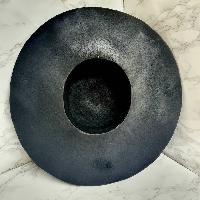 Puede incluir: Un sombrero negro de ala ancha hecho de fieltro. El sombrero tiene una corona grande y redonda y un ala ancha y plana.