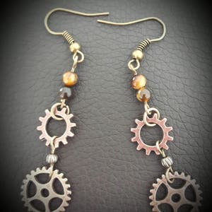 May include: A pair of gold tone earrings with tiger's eye beads and two different sized gear charms.
