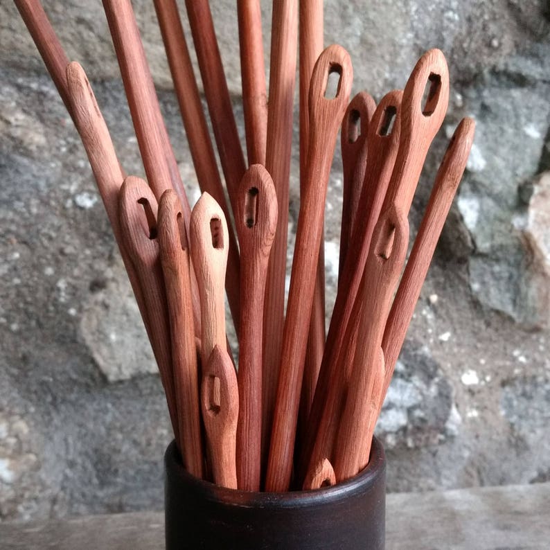 May include: A bunch of wooden knitting needles with a loop at the top, arranged in a brown ceramic container.