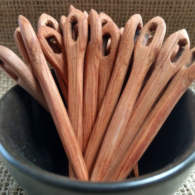 May include: A close-up of a bowl filled with wooden knitting needles. The needles are a reddish-brown color and have a smooth, polished finish.