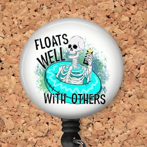 May include: A white retractable badge holder with a round button featuring a cartoon skeleton floating in a blue inflatable ring with a drink in its hand. The text on the button reads "Floats Well With Others".